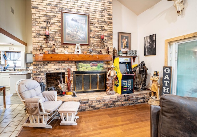 living room featuring a wealth of natural light, light hardwood / wood-style flooring, high vaulted ceiling, and a brick fireplace