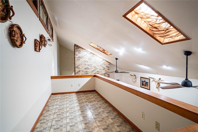 interior space with ceiling fan, vaulted ceiling with skylight, and brick wall