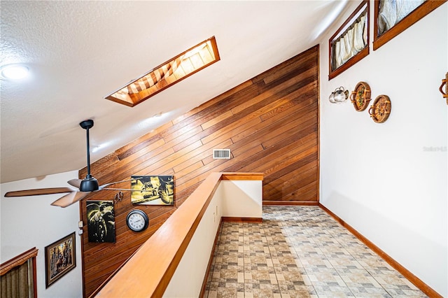 hall featuring lofted ceiling with skylight and wood walls