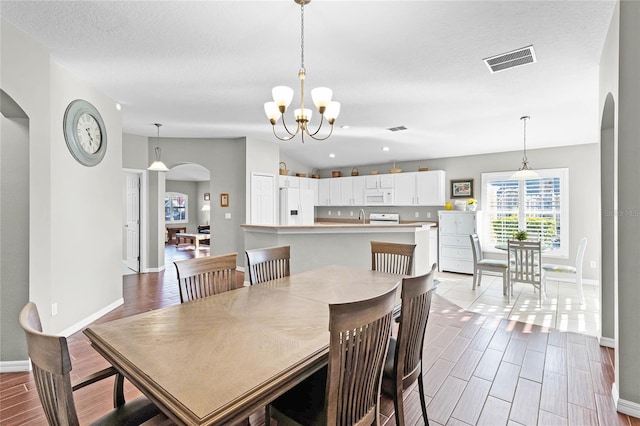 dining space with arched walkways, visible vents, a notable chandelier, and wood finish floors