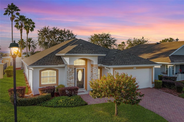 ranch-style home with a garage, roof with shingles, a lawn, and stucco siding