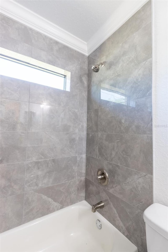 bathroom featuring tiled shower / bath combo, toilet, and ornamental molding