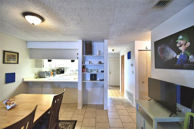 kitchen with kitchen peninsula, white cabinetry, light tile patterned flooring, and a textured ceiling