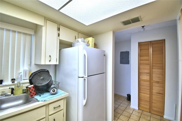 kitchen with white fridge, light tile patterned floors, sink, and cream cabinets