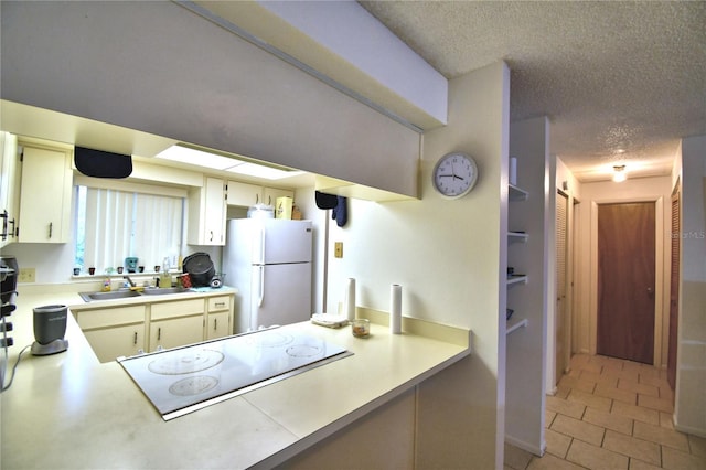 kitchen featuring sink, cream cabinets, white fridge, a textured ceiling, and black electric stovetop