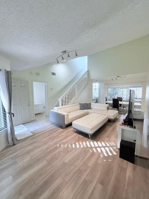 living room featuring a textured ceiling, light hardwood / wood-style floors, and lofted ceiling