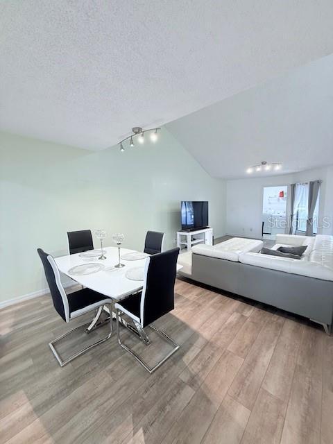 dining space with a textured ceiling, rail lighting, light hardwood / wood-style floors, and vaulted ceiling