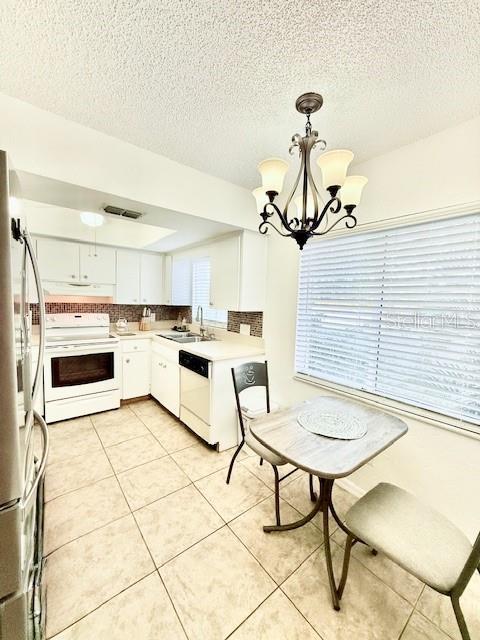 kitchen with decorative light fixtures, white cabinetry, white appliances, and a wealth of natural light