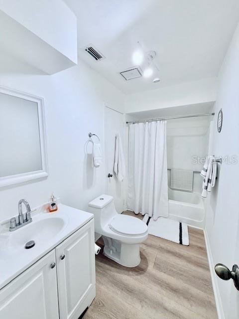 full bathroom with hardwood / wood-style floors, vanity, shower / tub combo, and toilet