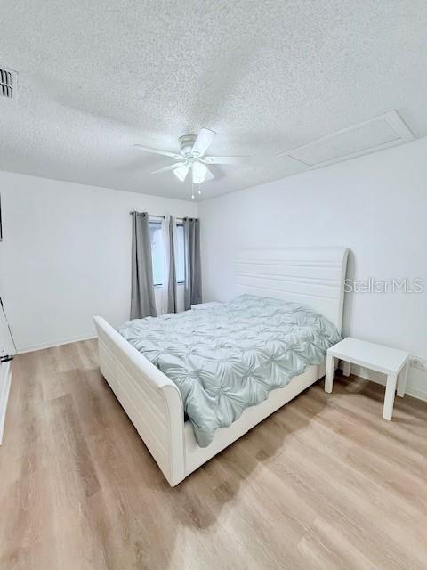 bedroom with a textured ceiling, light hardwood / wood-style floors, and ceiling fan