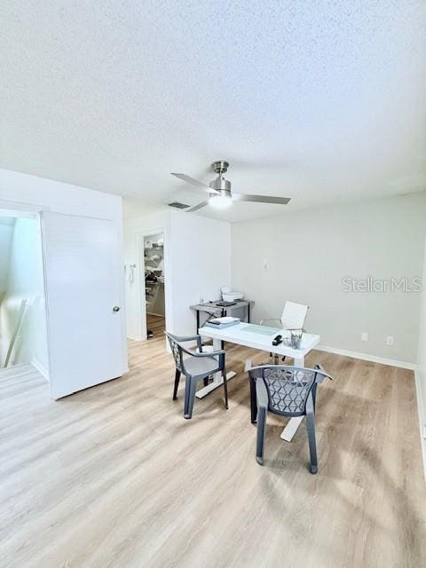 living area with ceiling fan, a textured ceiling, and light wood-type flooring