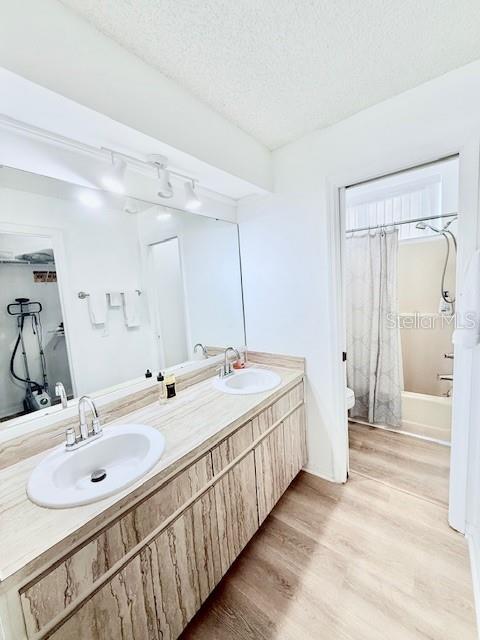 full bathroom with vanity, toilet, a textured ceiling, wood-type flooring, and shower / tub combo