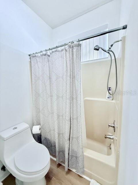 bathroom with hardwood / wood-style floors, toilet, and shower / bathtub combination with curtain