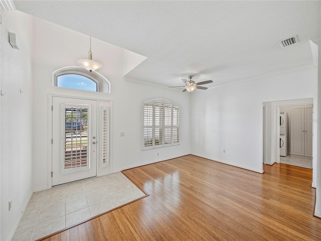 entryway with ceiling fan, stacked washer and dryer, a textured ceiling, and light wood-type flooring