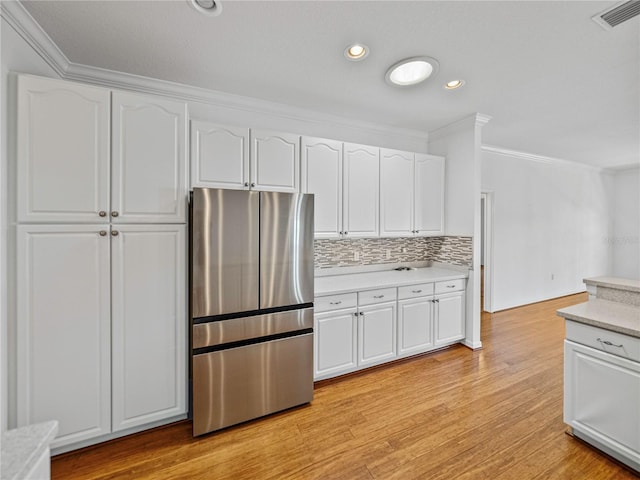 kitchen with stainless steel fridge, light wood-type flooring, white cabinetry, and ornamental molding