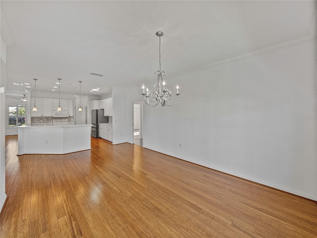 unfurnished living room with crown molding, light hardwood / wood-style flooring, and a notable chandelier