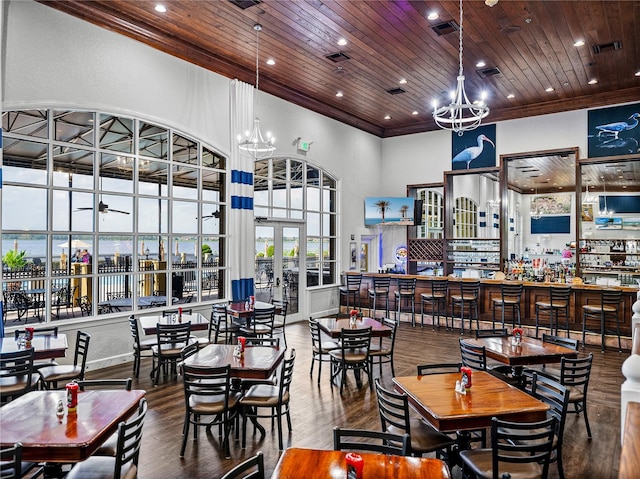 dining space featuring a towering ceiling, ornamental molding, wooden ceiling, a chandelier, and hardwood / wood-style floors