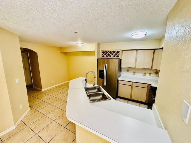 kitchen featuring stainless steel fridge, sink, light tile patterned floors, and a textured ceiling