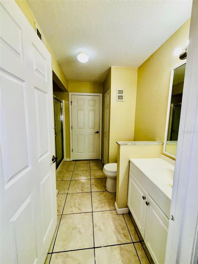 bathroom with tile patterned flooring, a textured ceiling, toilet, a shower with door, and vanity