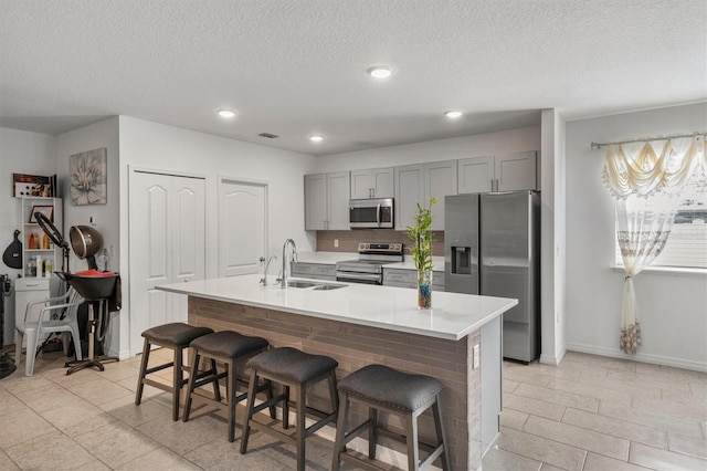 kitchen featuring sink, gray cabinets, an island with sink, a kitchen bar, and stainless steel appliances