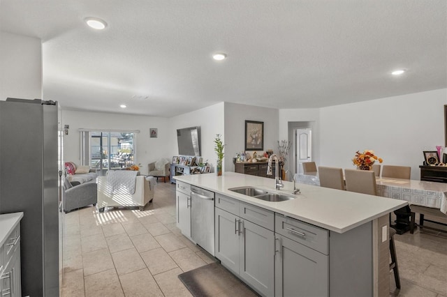 kitchen featuring a kitchen bar, gray cabinetry, sink, dishwasher, and an island with sink