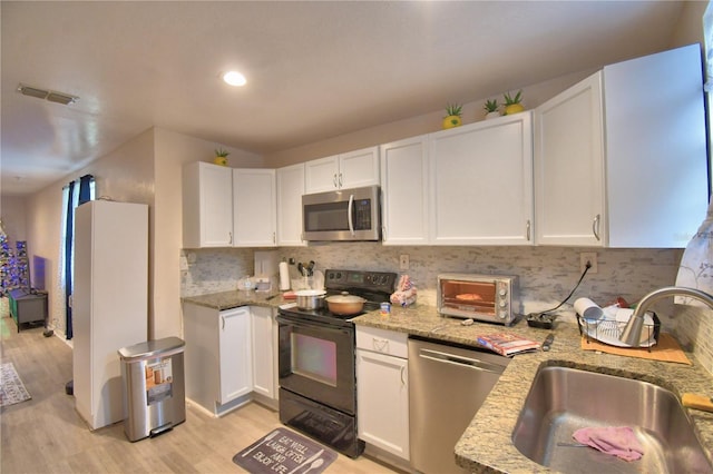 kitchen with white cabinetry, sink, light stone counters, appliances with stainless steel finishes, and light wood-type flooring