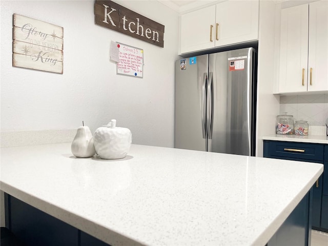 kitchen with light stone countertops, blue cabinets, stainless steel fridge, decorative backsplash, and white cabinets