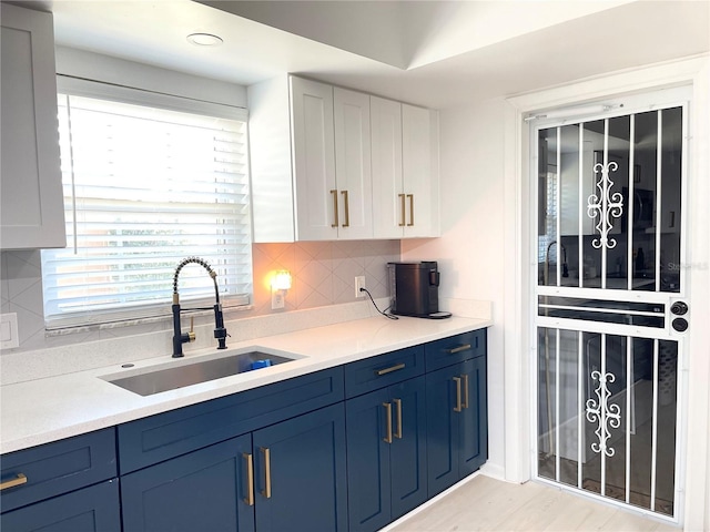 kitchen featuring backsplash, white cabinets, sink, light hardwood / wood-style flooring, and blue cabinetry