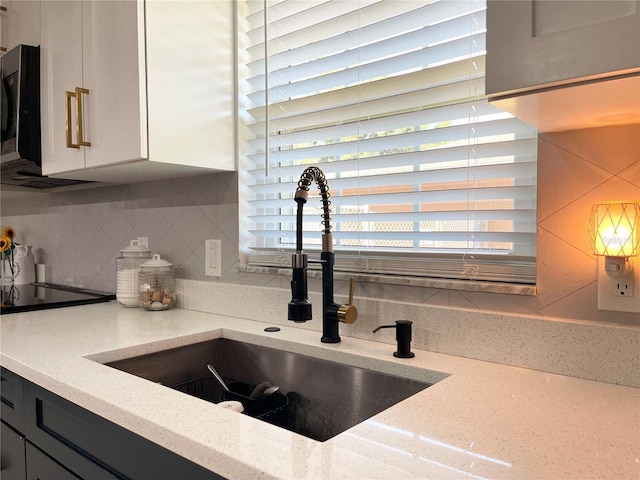 kitchen with light stone countertops, white cabinetry, sink, and tasteful backsplash