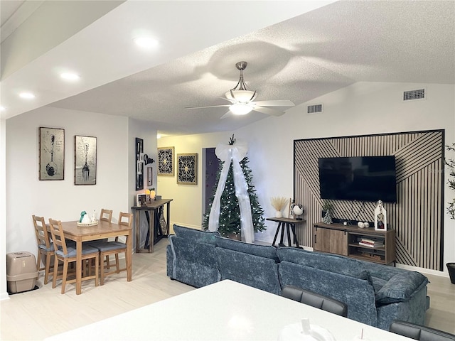 living room featuring ceiling fan, light wood-type flooring, a textured ceiling, and vaulted ceiling