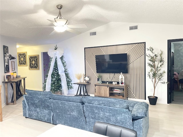 living room with a textured ceiling, ceiling fan, vaulted ceiling, and light wood-type flooring