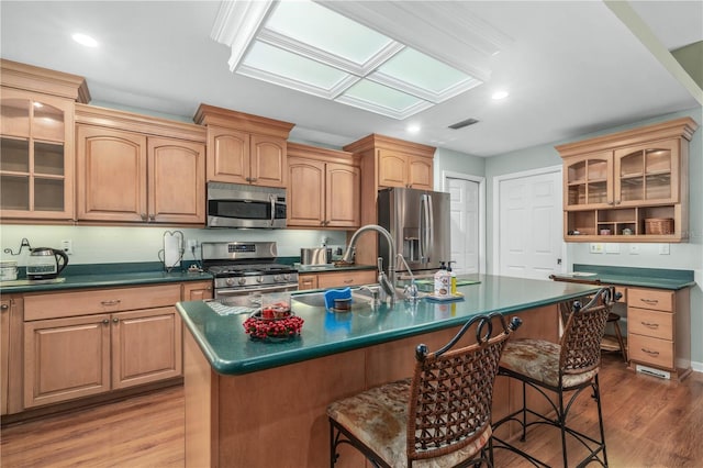 kitchen featuring appliances with stainless steel finishes, light hardwood / wood-style floors, a kitchen breakfast bar, and an island with sink