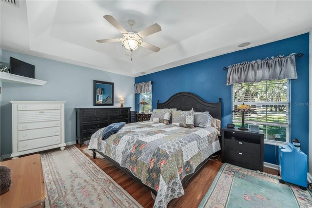 bedroom featuring ceiling fan, dark wood-type flooring, and a tray ceiling