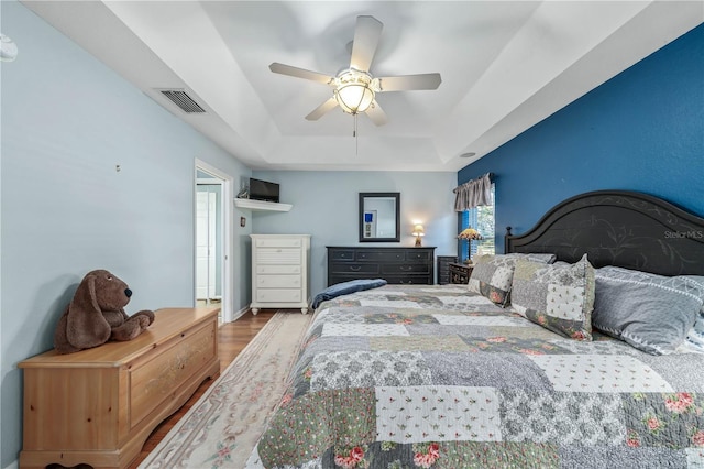 bedroom featuring hardwood / wood-style floors, ceiling fan, a raised ceiling, and multiple windows