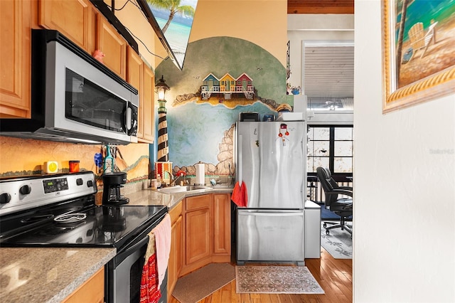 kitchen featuring appliances with stainless steel finishes, light wood-type flooring, light stone counters, and sink