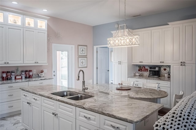 kitchen featuring white cabinetry, a kitchen island with sink, sink, and hanging light fixtures