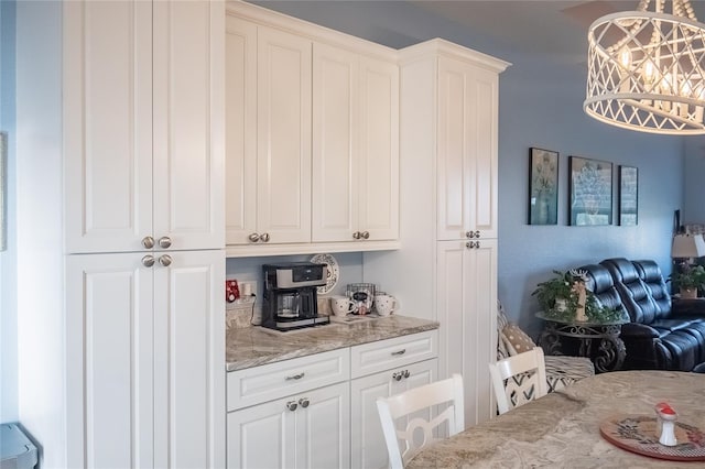 kitchen with light stone counters, white cabinetry, and hanging light fixtures