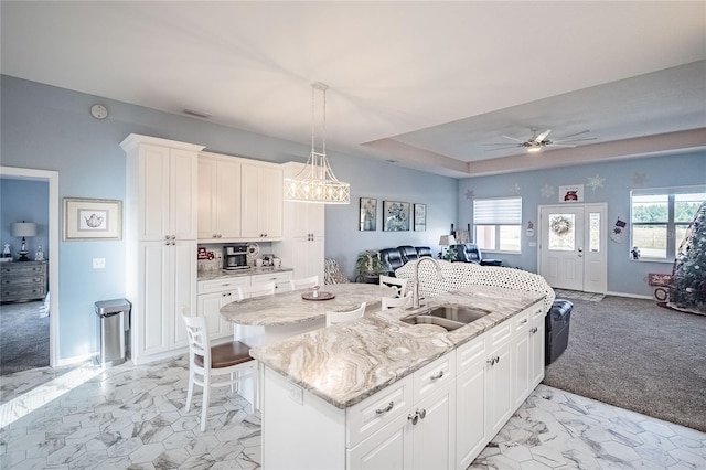 kitchen with light carpet, sink, white cabinets, and an island with sink