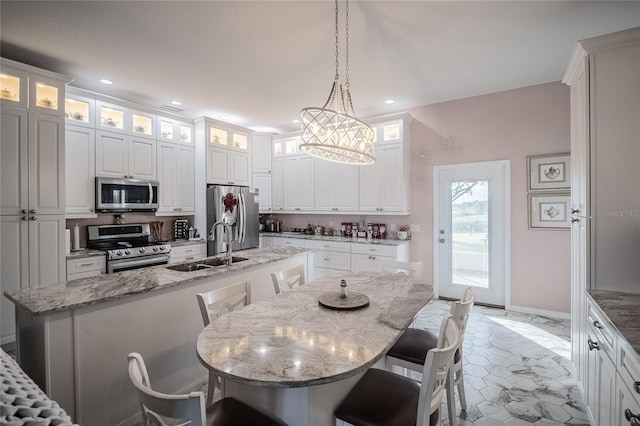 kitchen featuring stainless steel appliances, light stone counters, an island with sink, pendant lighting, and a breakfast bar area