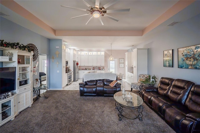 living room featuring a tray ceiling, light carpet, and ceiling fan