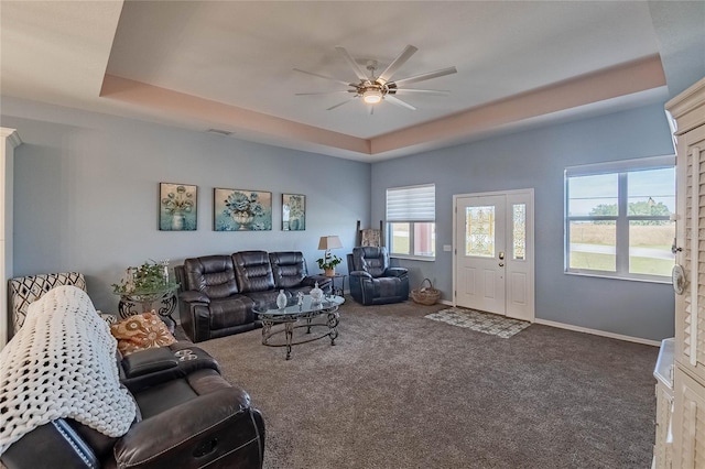 carpeted living room with a raised ceiling and ceiling fan