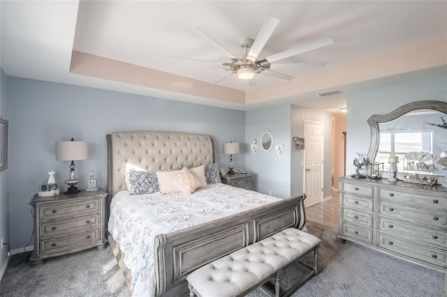 bedroom with a raised ceiling, ceiling fan, and dark carpet