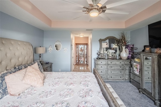 carpeted bedroom with a raised ceiling and ceiling fan