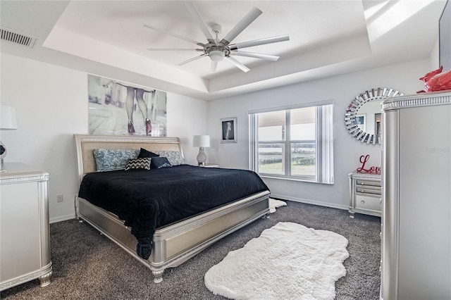 bedroom with ceiling fan, dark carpet, and a raised ceiling