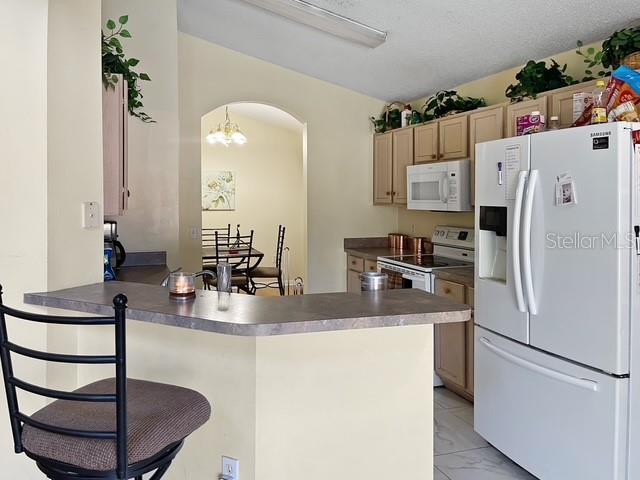 kitchen featuring light brown cabinets, an inviting chandelier, kitchen peninsula, white appliances, and a kitchen bar