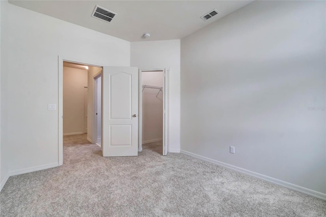 unfurnished bedroom with a walk in closet, light carpet, and a closet