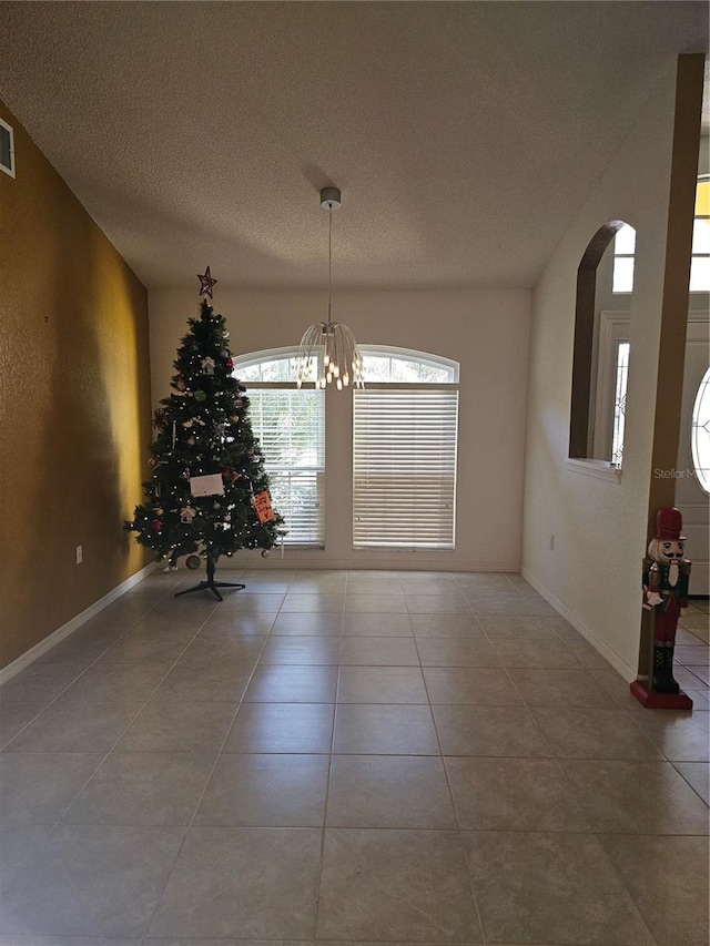 unfurnished dining area with tile patterned floors, a textured ceiling, and a notable chandelier