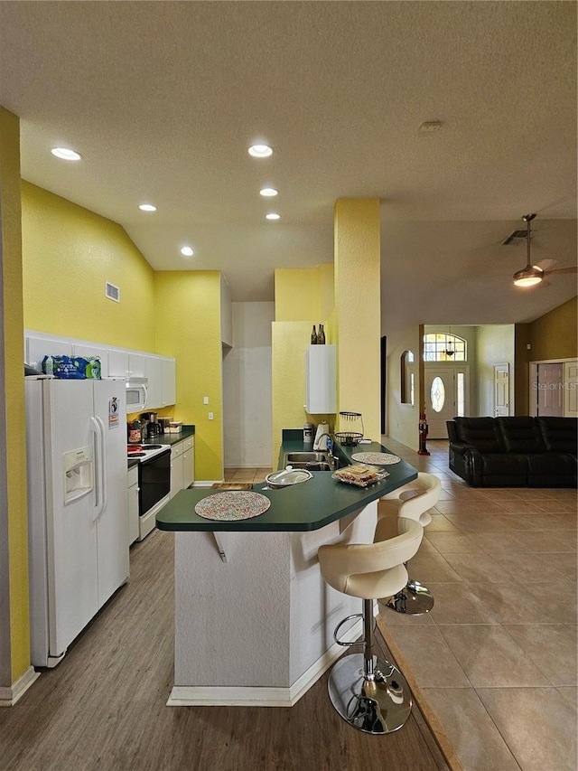 kitchen featuring a breakfast bar, a textured ceiling, white appliances, light hardwood / wood-style flooring, and white cabinetry