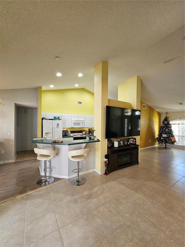 kitchen with lofted ceiling, white appliances, kitchen peninsula, a kitchen bar, and white cabinetry