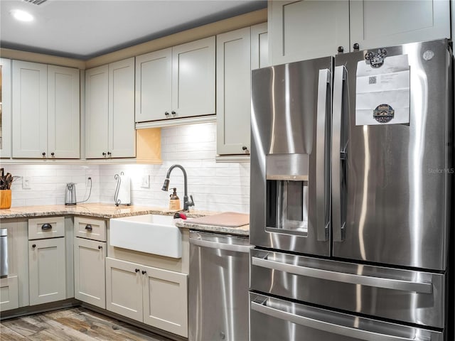 kitchen featuring light stone countertops, appliances with stainless steel finishes, backsplash, sink, and light hardwood / wood-style flooring